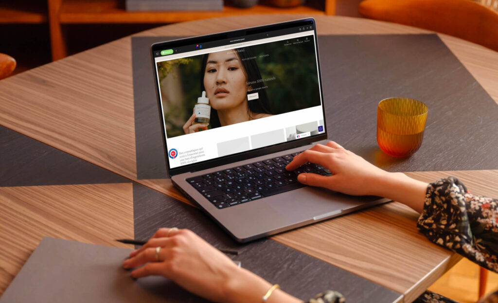Personne naviguant sur la page d’accueil de la boutique Minimaliste depuis un ordinateur portable, avec la photo d’une femme tenant un flacon de sérum
