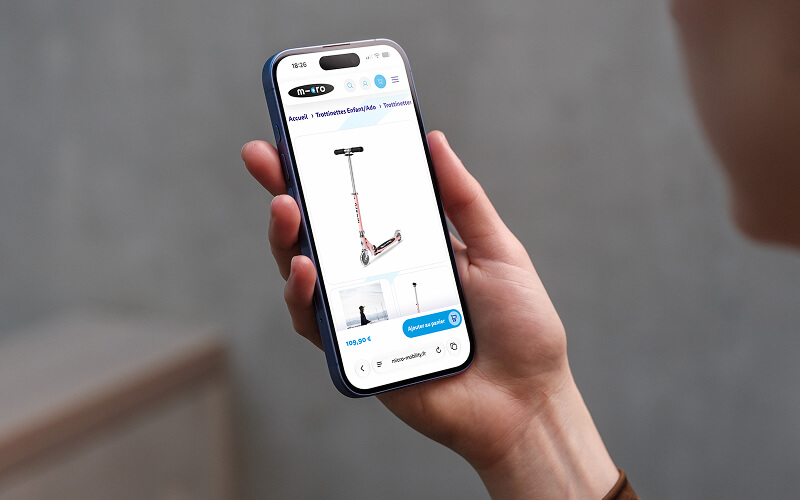 Person holds a smartphone displaying a product page for a red-and-gray kick scooter sold online, front view on the screen.