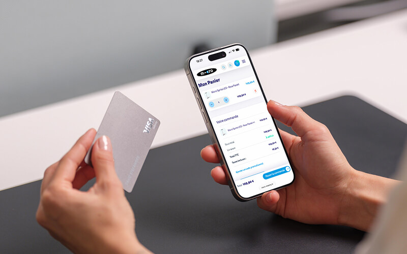 Hands hold a silver credit card in one hand and a smartphone displaying a banking app with a list of transactions in the other hand.